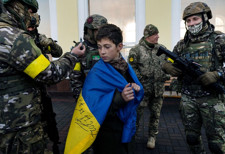 Un joven pide a soldados ucranianos que le autografíen la bandera que llevaba como capa mientras espera el primer tren desde Kiev, la capital de Ucrania, para hacer el viaje a Kherson desde antes de que comenzara la invasión rusa, el 19 de noviembre de 2022. Ucrania reconquistó Kherson y despejó la orilla occidental del Dnipro. Pero la ofensiva se detuvo allí. (Lynsey Addario/The New York Times)