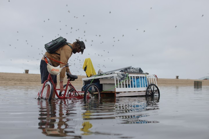 Un hombre ajusta su carga mientras pasea en bicicleta por un sendero inundado tras las fuertes lluvias del martes 14 de octubre de 2025 en Santa Mónica, California. Foto AP